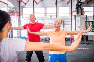 Oudere vrouw en man doen oefeningen in sportzaal.